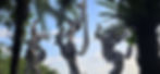 Three ornate goddess statues with flowing hair stand among tropical palms against a blue sky, creating a dramatic, serene scene.