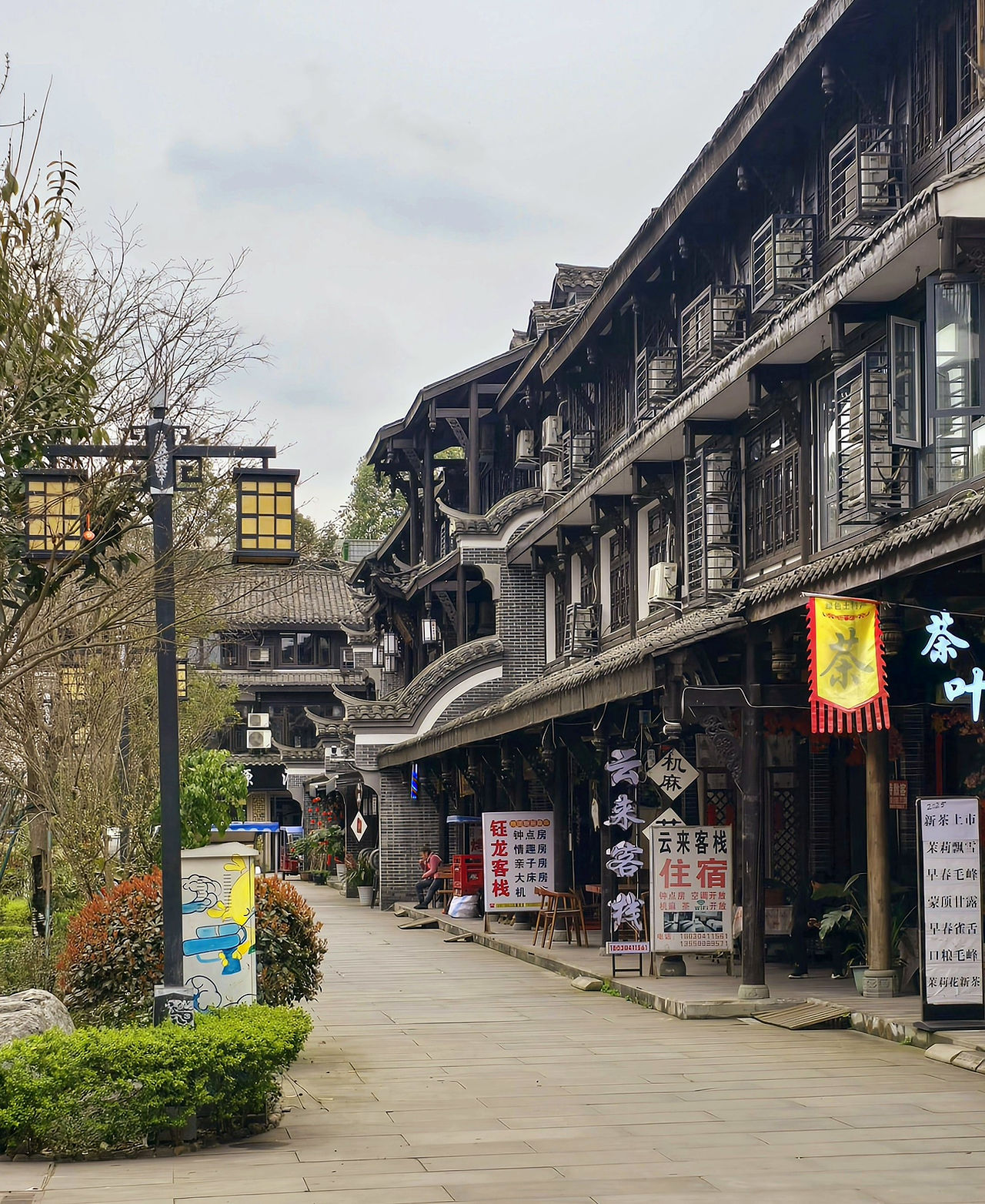 A side view of a traditional wooden store, with multiple modern signs out the front, 2 yellow street lights, clean cobbled path