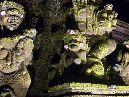 Three moss-covered stone figures adorned with pink flowers in a dimly lit setting, exuding a mysterious and ancient aura.