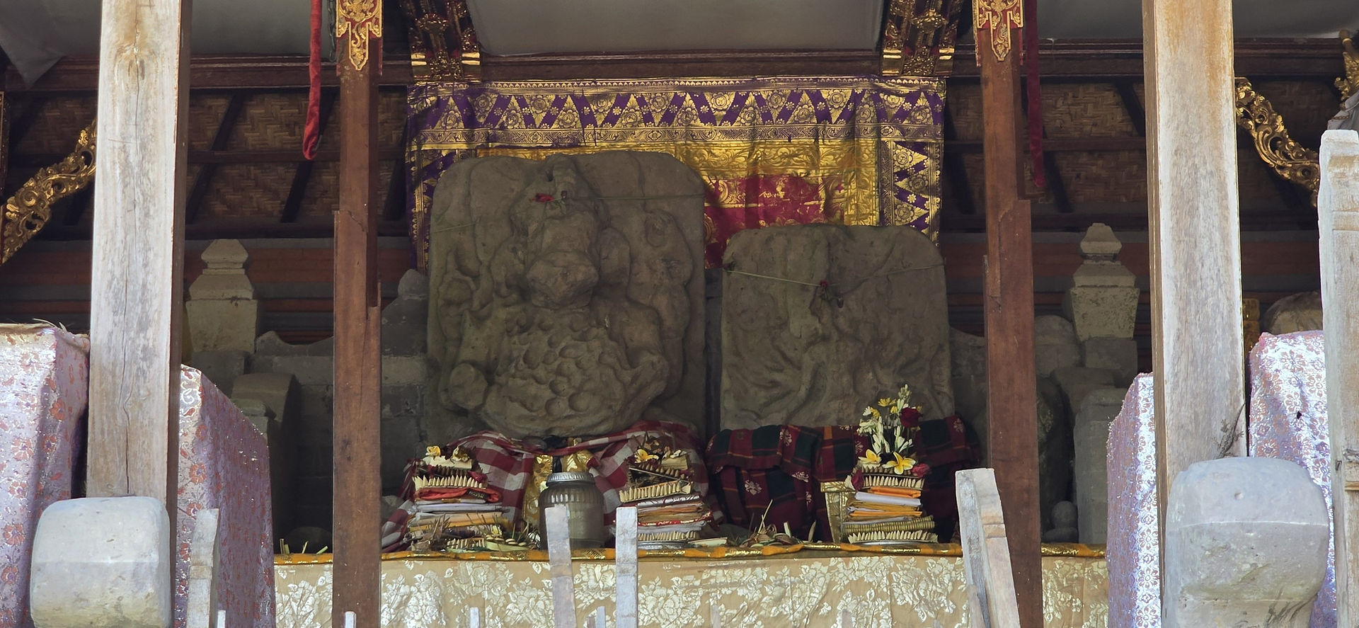 Stone statues in a temple adorned with colourful cloth and offerings. Gold and purple tapestry in the background. Calm and sacred ambiance.