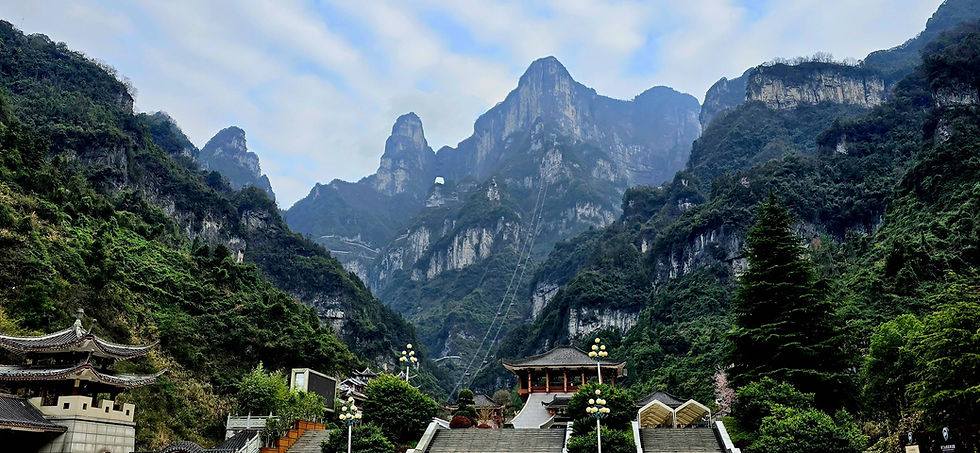 Mountain landscape with lush green valleys and a traditional temple in the foreground. Staircase and lampposts lead to the temple.