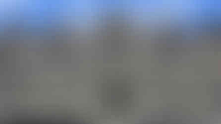 Stone temple facade with intricate carvings and Buddha statues set in niches. The weathered stone is gray and beige against a blue sky.