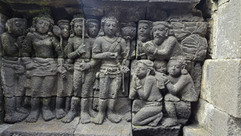 Stone relief depicts six seated figures with detailed headdresses, set against a floral-patterned stone background, exuding a serene vibe.