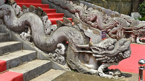 Stone dragon sculptures line red-carpeted steps with greenery in the background. Weathered texture adds a historic feel.