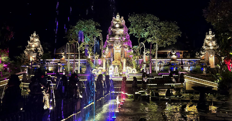 Night scene of a temple in Ubud with colourful lights illuminating intricate carvings, water reflections and silhouetted trees.
