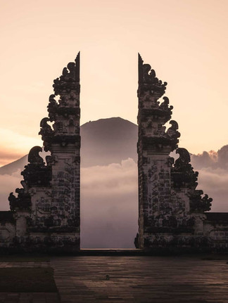 Ancient split stone gate frames a misty mountain at sunrise, with warm pink sky and dark carved silhouettes.