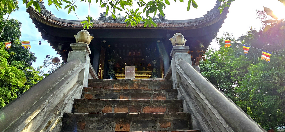 Stone steps lead up to a pagoda entrance adorned with flags. Green foliage surrounds the scene. A peaceful atmosphere prevails.