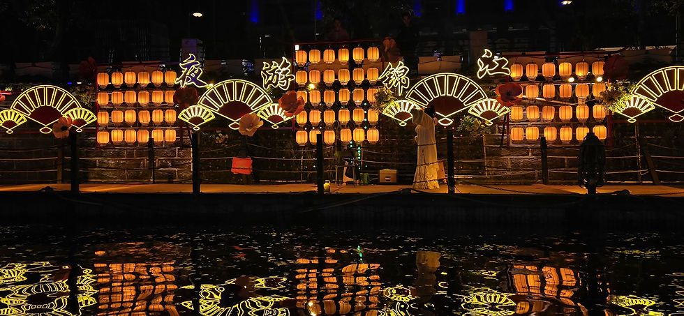 Bright lanterns and neon fans glow against a dark backdrop, reflecting in the water. Chinese characters are illuminated, creating a festive mood.