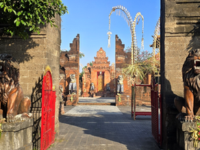 Stone temple gate with red doors and roaring lion statues, leading to a Balinese shrine under blue sky