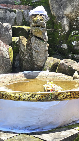 Stone turtle sculptures beside a water basin adorned with a gold-patterned cloth. Yellow fabric with woven decorations is in the background.