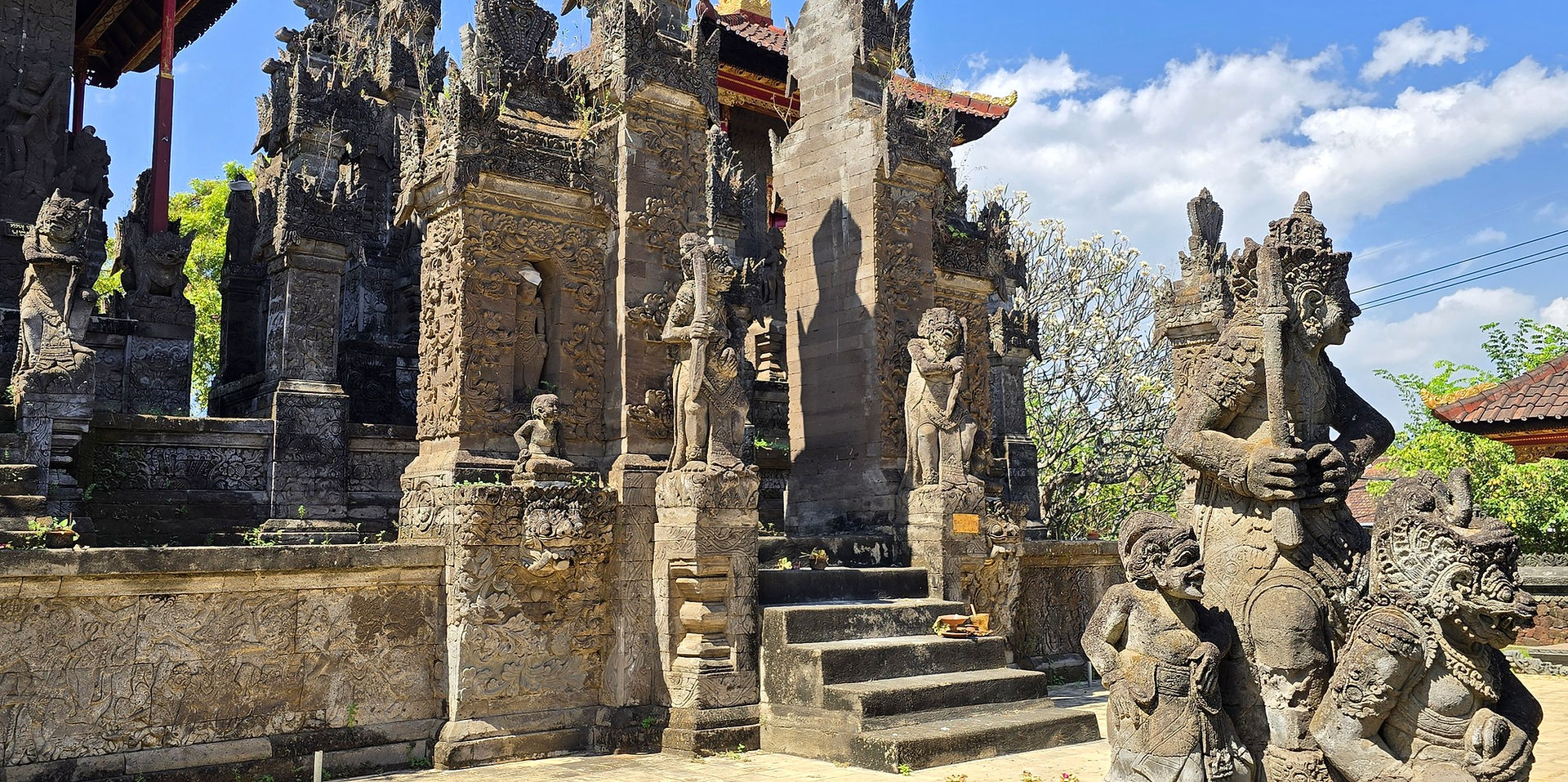 Intricately carved stone temple with guardian statues and steps under a bright blue sky, sunlit and serene.