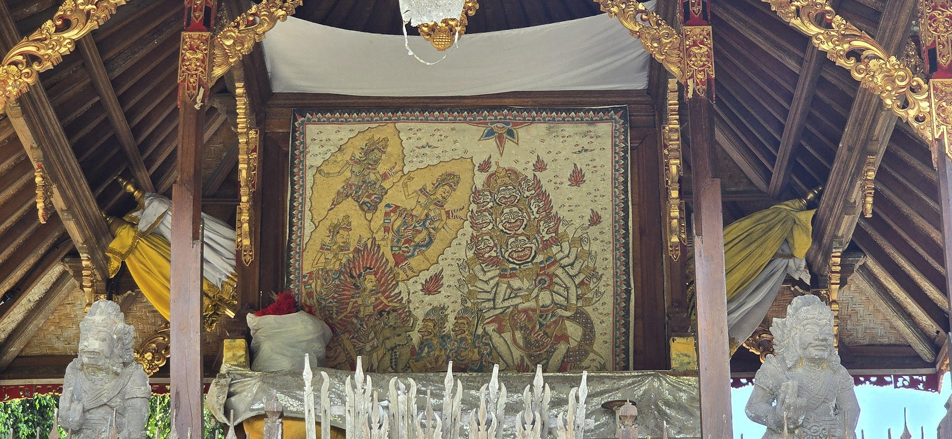 Ornate wooden shrine with intricate, colourful tapestry depicting mythological figures. Stone statues adorn the structure.