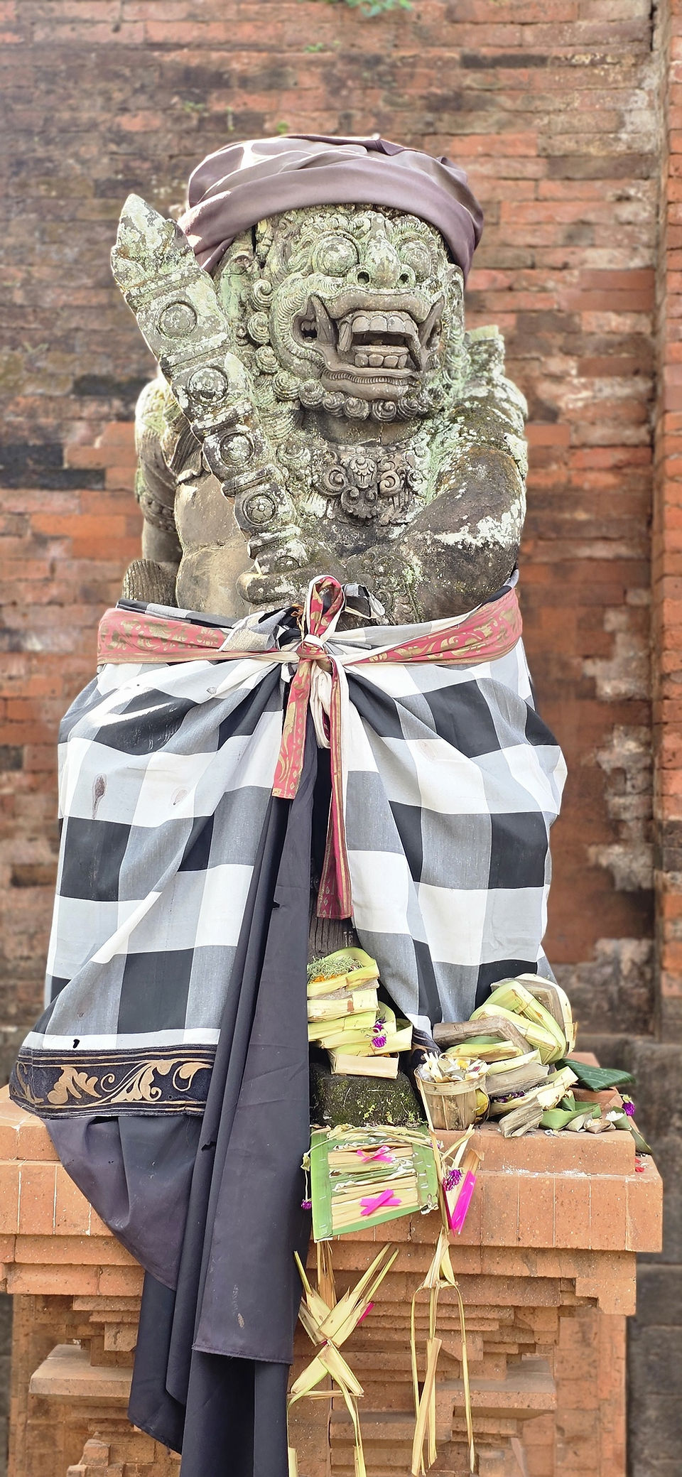 Weathered guardian sculpture with fierce expression wearing a poleng sarong at a historic Balinese royal palace