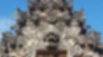 Ornate stone temple facade with intricate carvings of mythical creatures against a clear blue sky; detailed textures and patterns.