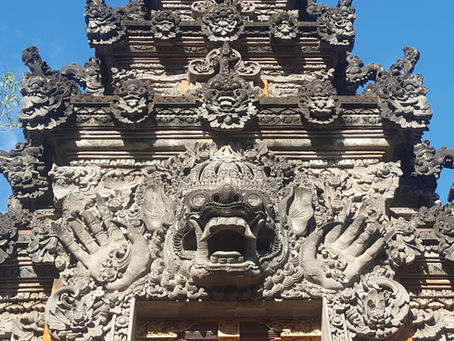 Ornate stone temple facade with intricate carvings of mythical creatures against a clear blue sky; detailed textures and patterns.