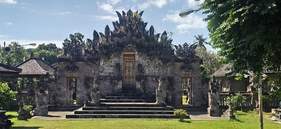 Ornate stone temple with steps, carved black spires, and a gold door amid tropical greenery under a blue sky.
