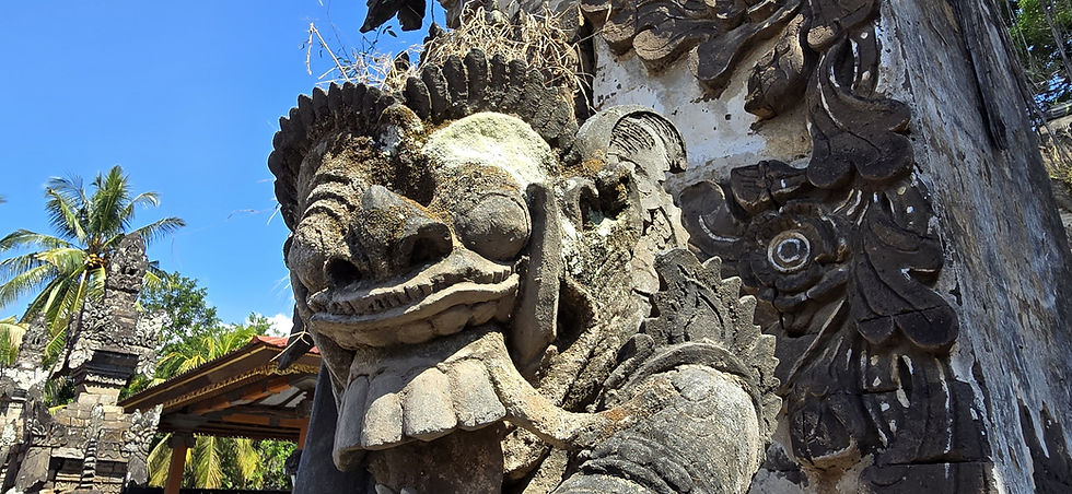 Close up of weathered stone guardian face at a tropical temple, with palm trees and blue sky in bright sunlight.