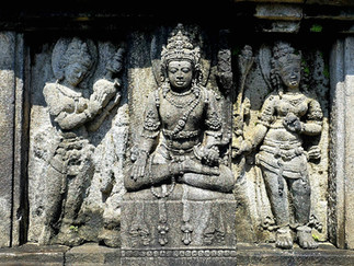 Stone carvings of three figures, with the central figure seated in meditation, flanked by two standing figures, all ornately detailed.