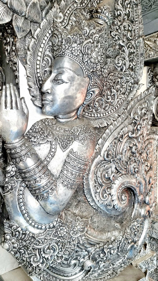 Elaborate figure of a deity in prayer pose, adorned with ornate silver headdress