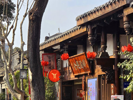 Historic Chinese street scene with traditional wooden buildings, red lanterns and bare trees. Bright, sunny day; text on signs in Chinese.