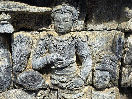 Ancient stone relief depicting a serene figure with ornate attire in a historical setting. The stone texture is detailed and weathered.