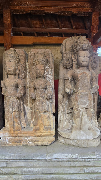 Three weathered stone guardian statues stand in a wooden temple alcove, serene and ancient.