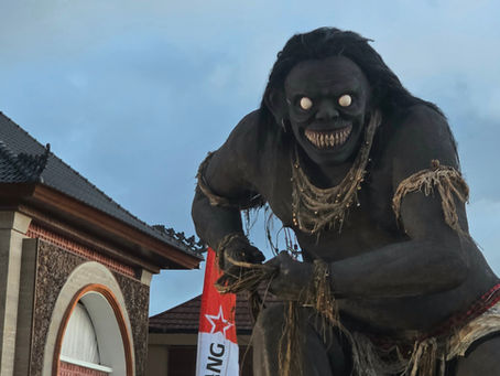 Giant black demon statue with glowing eyes and sharp teeth looming over a temple-like building, with red banners