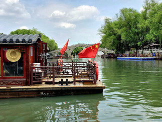 Bright reflections in Suzhou’s clear canal water, mirroring traditional boats, green river surrounded by green trees