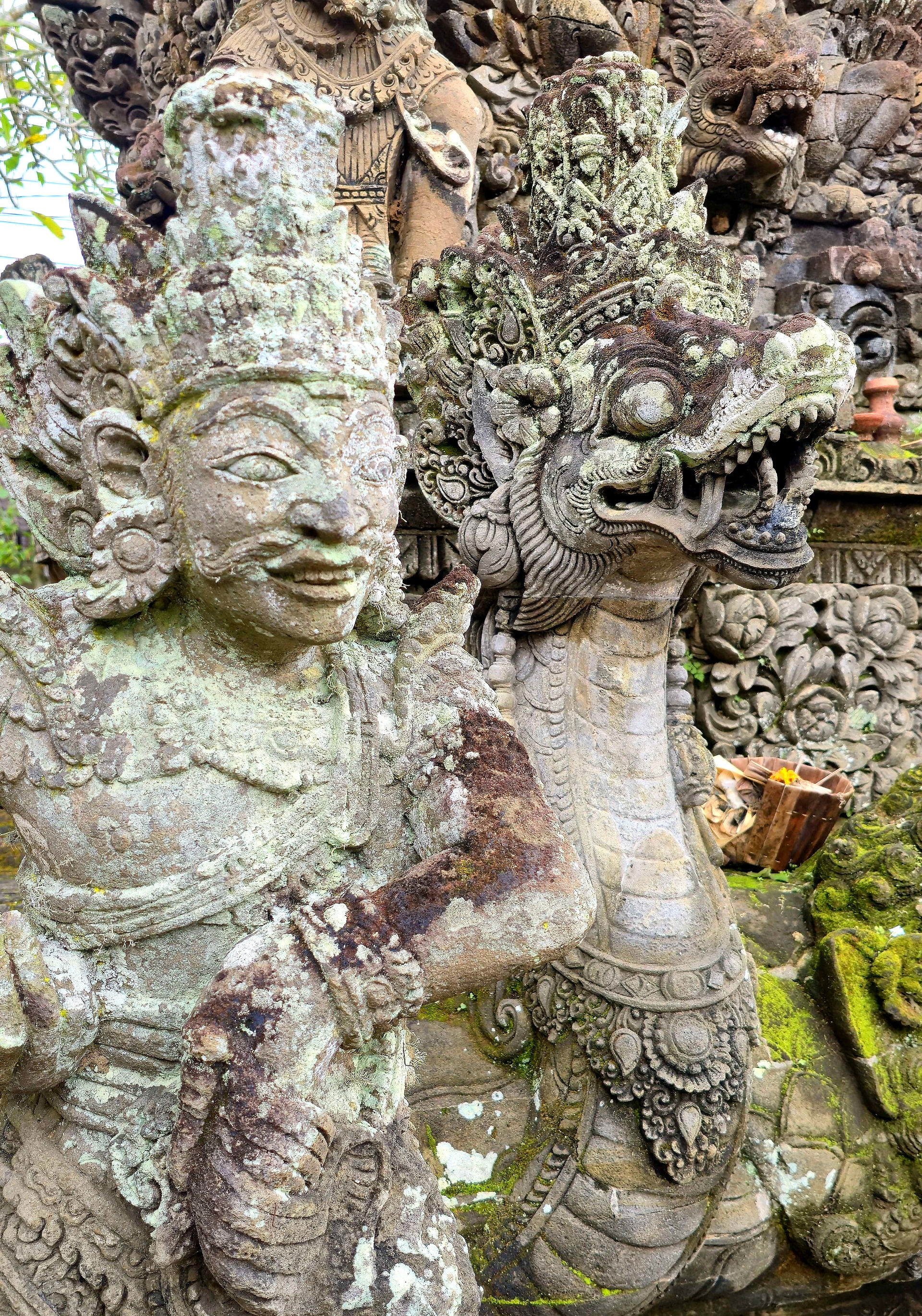 Intricately carved stone statues of a deity and mythical creature with moss in a decorative setting. Rich textures and earthy tones.