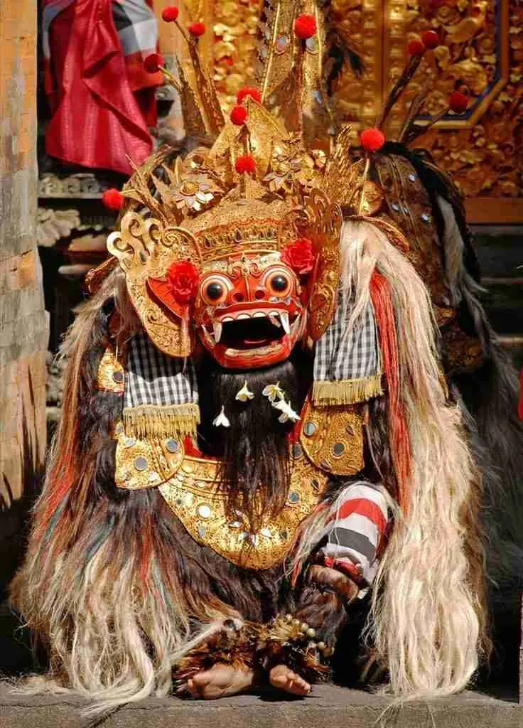 Colourful Balinese Barong costume with ornate gold and red details, long fur, in front of a decorated background, exuding vibrant energy.