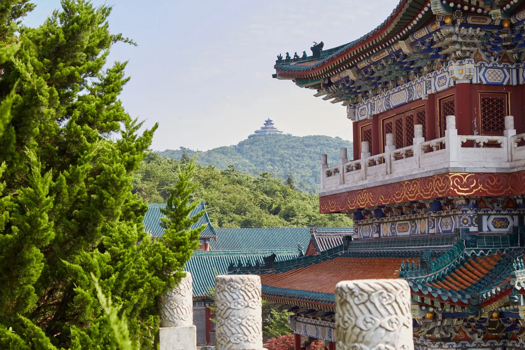 side view of the red and white temple, mountains in the background, green pine trees