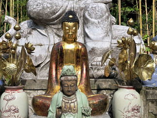 Gold and green Buddha statues surrounded by blue statues and gold floral sculptures in a serene bamboo garden setting.