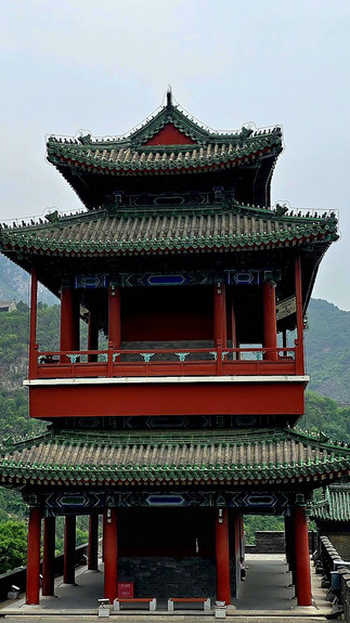ancient red arrow multi-tiered tower with ornate green tiled roofs, green mountains in the background, overcast