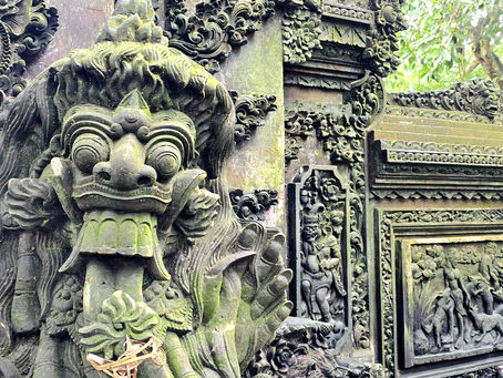 Ornate stone carvings of mythical creatures and figures on a green-tinged temple wall, surrounded by lush foliage.