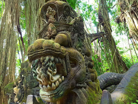Ancient stone serpent statue with intricate carvings in a lush jungle setting, surrounded by dense green foliage and hanging tree roots.