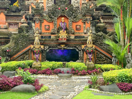 Ornate Balinese temple features intricate carvings, vibrant greenery, and statues. Lush garden path leads to "Puri Langon" entrance.