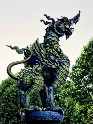 A vibrant green and blue dragon statue stands majestically against a backdrop of lush greenery, exuding a mythical and powerful presence.