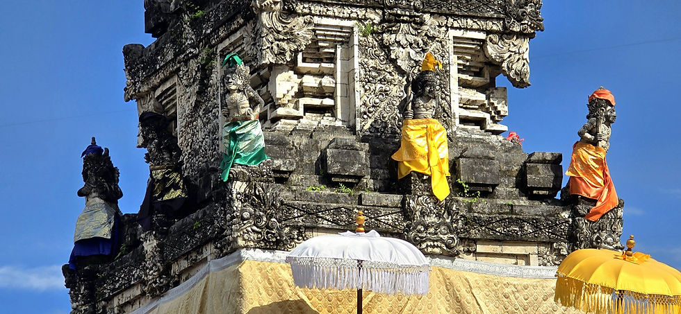Ornate stone statues in vibrant green, yellow, and orange attire adorn a temple facade under a clear blue sky. Decorative umbrellas below.