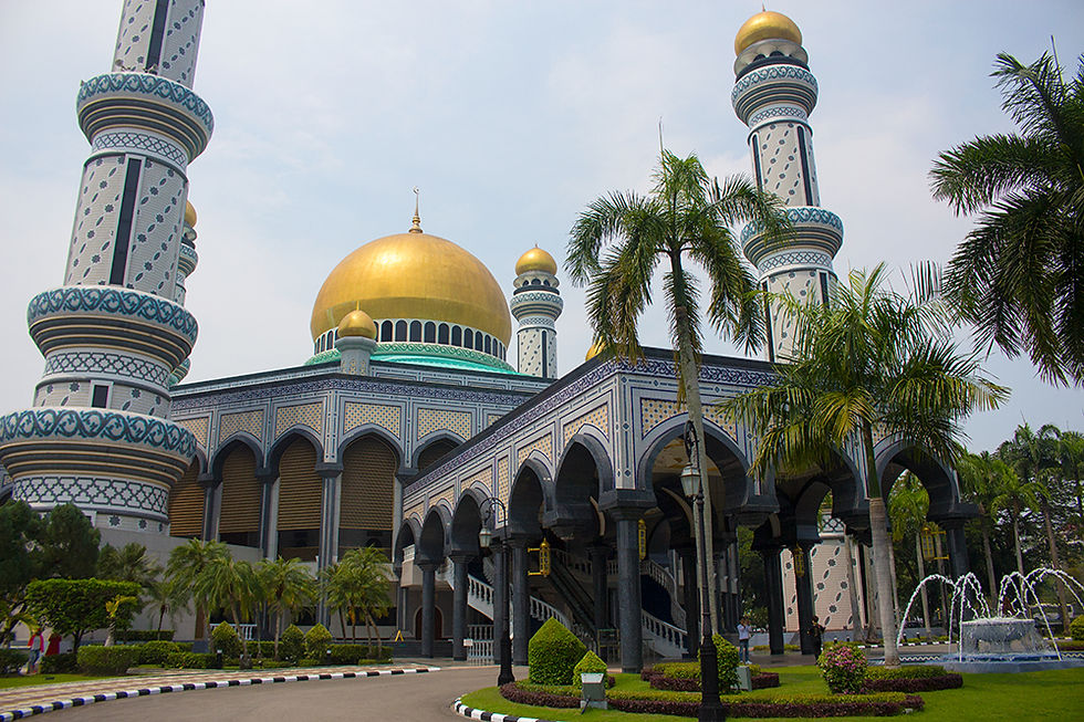 Ornate mosque with a golden dome, towering minarets, and arched entrance. Palm trees and fountains in the foreground, clear sky above.