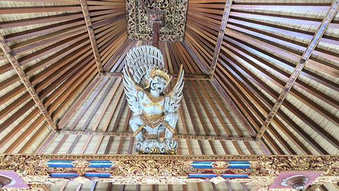 Ornate temple ceiling with a white-and-gold winged guardian statue, carved wood beams, and decorative red, blue, and gold trim
