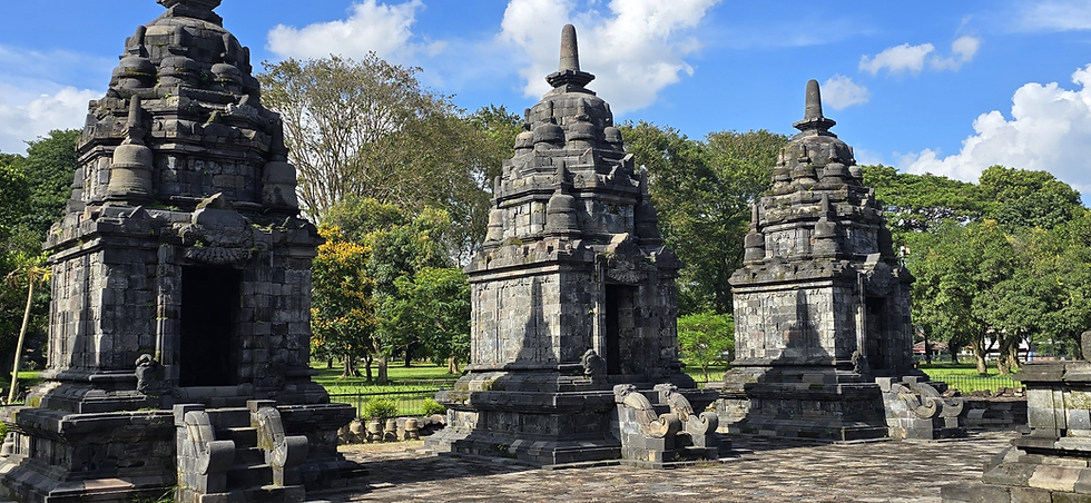 Stone temples under a blue sky with fluffy clouds. Green trees and yellow flowers surround the ancient structure, creating a peaceful scene.