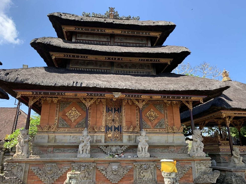 Balinese temple with intricate carvings, statues, and a thatched roof. Bright blue sky and lush greenery. Peaceful and ornate setting.