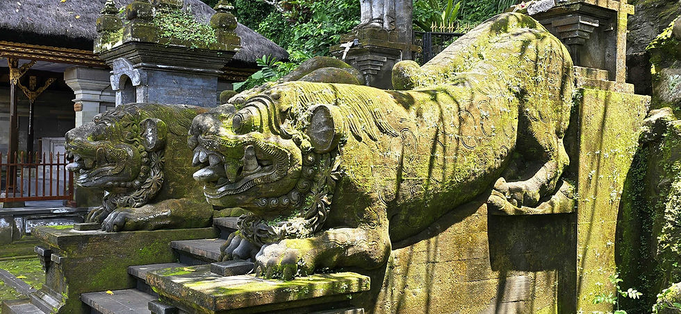 Moss-covered stone lion statues guard a temple entrance, surrounded by lush greenery. Sunlight creates contrasting shadows.