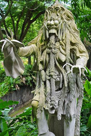 Grotesque leyak figure in stone, mid-transformation with exposed tongue and contorted limbs, mossy, jungle background