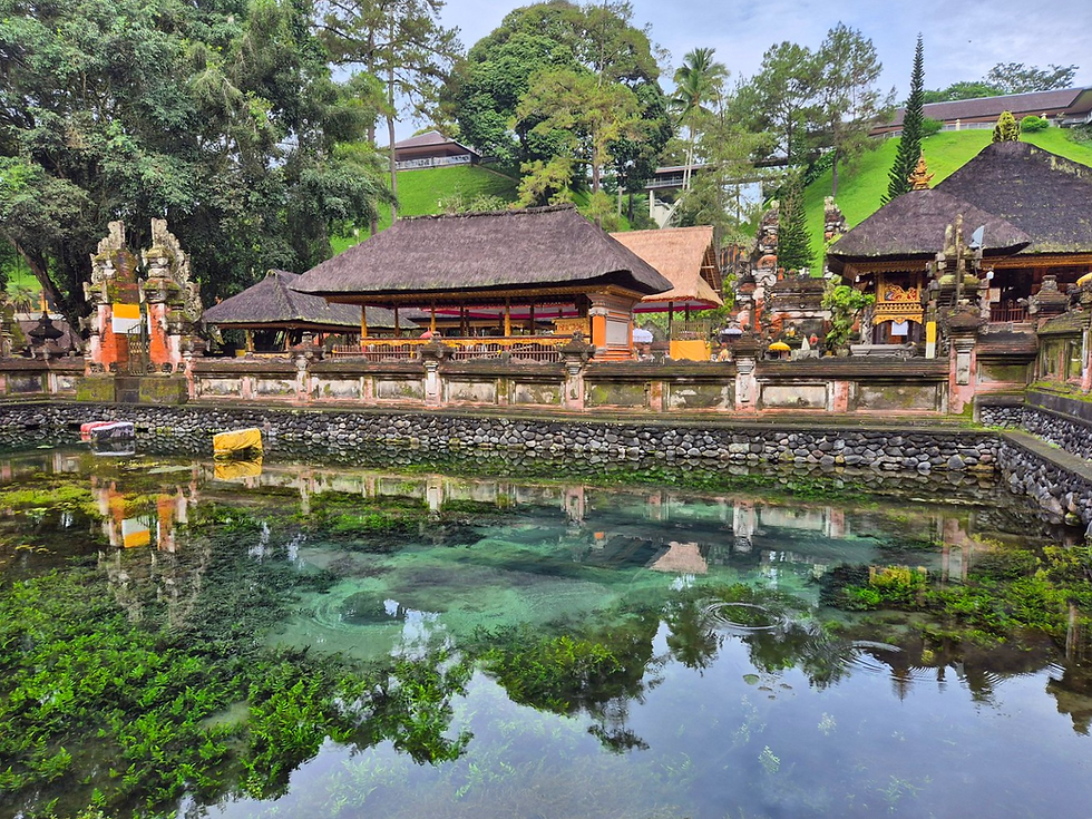 Serene temple with ornate structures and thatched roofs by a clear, reflective pond. Lush greenery surrounds the area, creating tranquility.