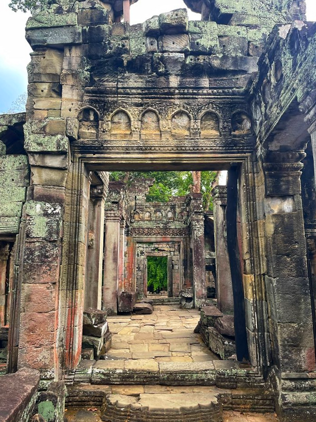 Dimly lit corridor inside Preah Khan, with moss-covered walls and long shadows creating a mysterious, ancient atmosphere.