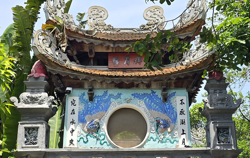 Ornate Asian temple gate with intricate carvings, blue dragon murals, and Chinese characters. Surrounded by lush green foliage. Calm setting.