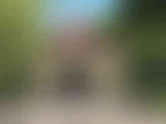 A serene temple with a red-tiled roof, surrounded by lush greenery. Stone statues and intricate carvings are visible in the foreground.