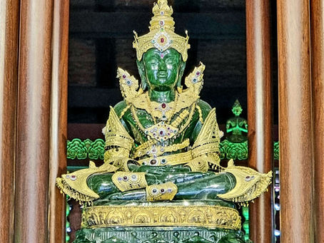Emerald Buddha statue adorned with gold and jewels, seated in a wooden temple with intricate patterns, evoking a serene, regal atmosphere.