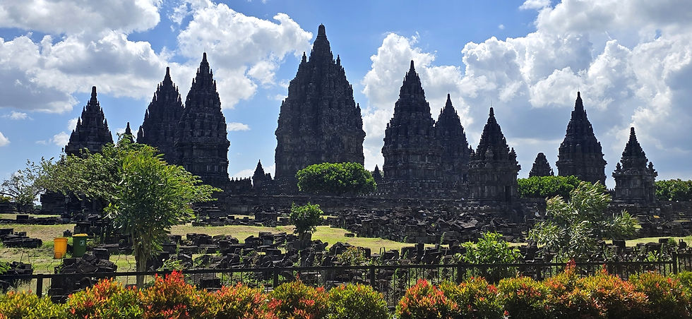 Ancient temple spires under a bright blue sky with clouds. Greenery and colourful plants in the foreground, creating a serene atmosphere.